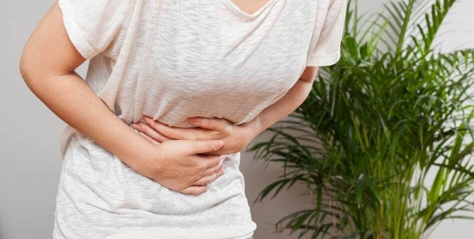 A woman is holding her stomach in pain, seeking relief and ways to improve her digestive system.