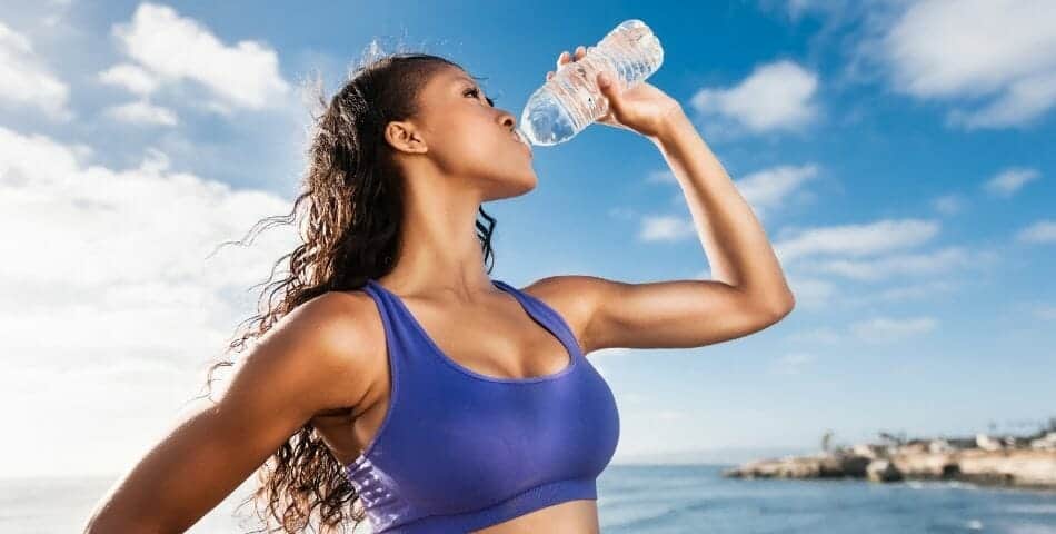 A woman hydrating on the beach - drink more water for better health - Metabolix health